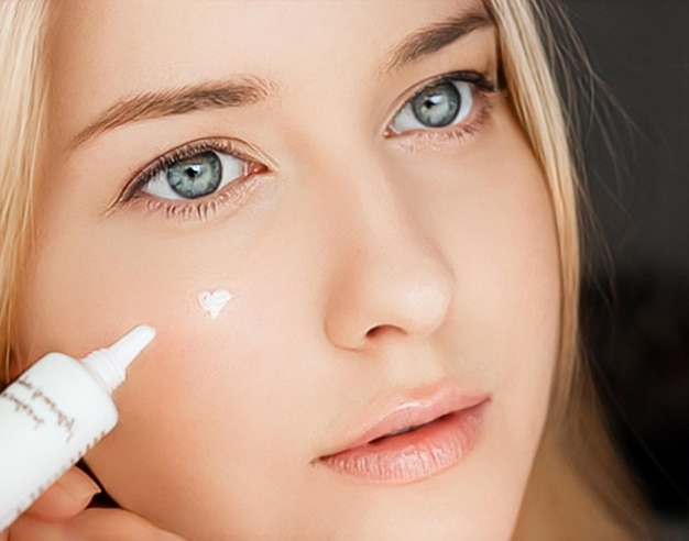 Hermosa mujer aplicando crema para el cuidado de la piel en la cara