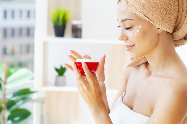 Hermosa mujer aplicando crema humectante en su rostro.