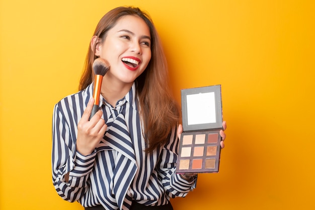 Hermosa mujer artista de maquillaje es feliz sobre fondo amarillo