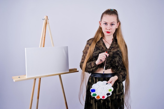 Hermosa mujer artista pintora con pinceles y lienzo al óleo posando en estudio aislado en blanco