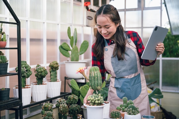 Hermosa mujer de Asia propietaria de una pequeña empresa usa tableta en una pequeña tienda de cactus