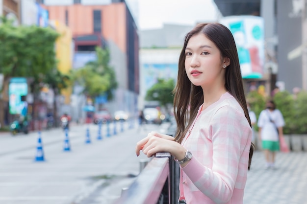 Hermosa mujer asiática con un abrigo de rayas rosa y blanco está de pie al aire libre urbano con la ciudad y la carretera como fondo.