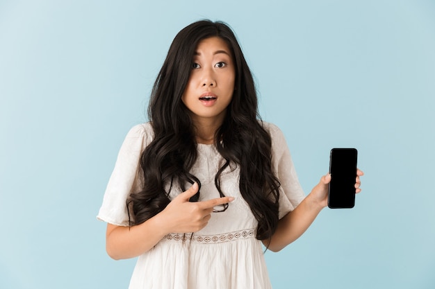 Hermosa mujer asiática aislada sobre pared azul que muestra la pantalla del teléfono móvil