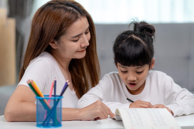 Una hermosa mujer asiática ayudando a su hija con la tarea en casa.