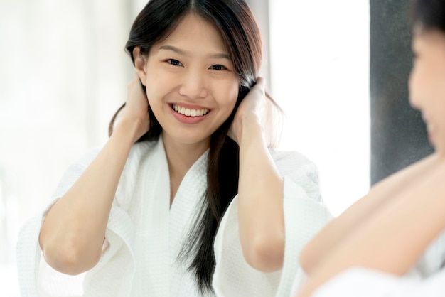 Hermosa mujer asiática bañándose cepillo para el cabello y vestido con espejo reflectante fondo de baño