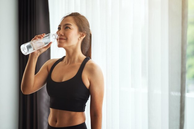 Una hermosa mujer asiática bebiendo agua de una botella de plástico mientras hace ejercicio