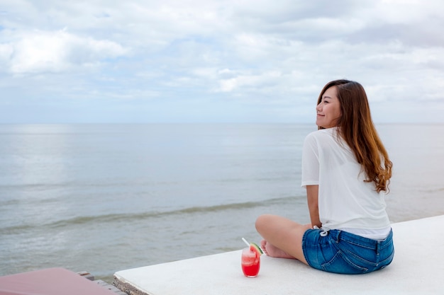 Foto una hermosa mujer asiática bebiendo jugo de sandía mientras está sentado junto al mar