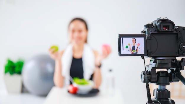 Foto hermosa mujer asiática blogger saludable está mostrando frutas y alimentos dietéticos limpios frente a la cámara para grabar video vlog en vivo en casa.