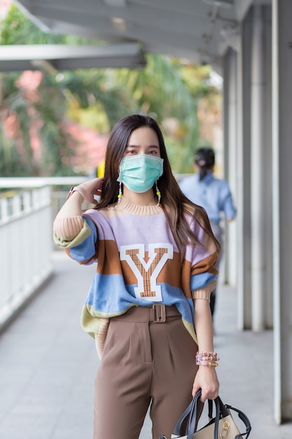 Hermosa mujer asiática caminando en la ciudad usa suéteres coloridos cabello largo y máscaras médicas