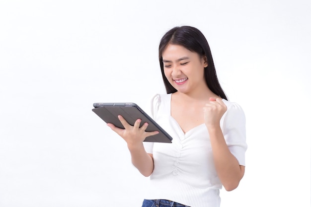 Hermosa mujer asiática en camisa blanca está feliz y satisfecha mientras mira en la tableta en su mano