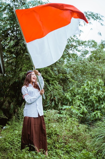 Una hermosa mujer asiática con camisa blanca y falda marrón ondeando la bandera en su mano y