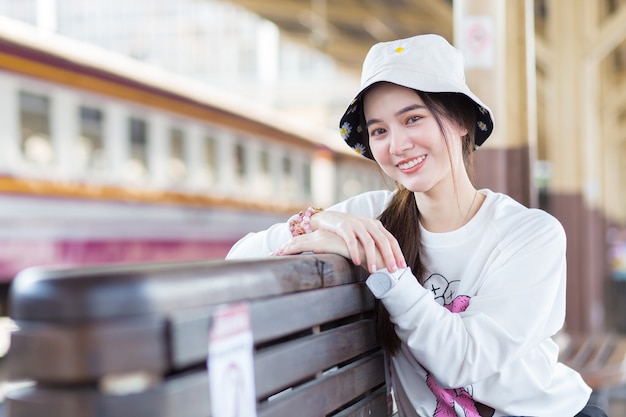 Hermosa mujer asiática en una camisa blanca de manga larga y un sombrero se sienta feliz smilie en la estación de tren