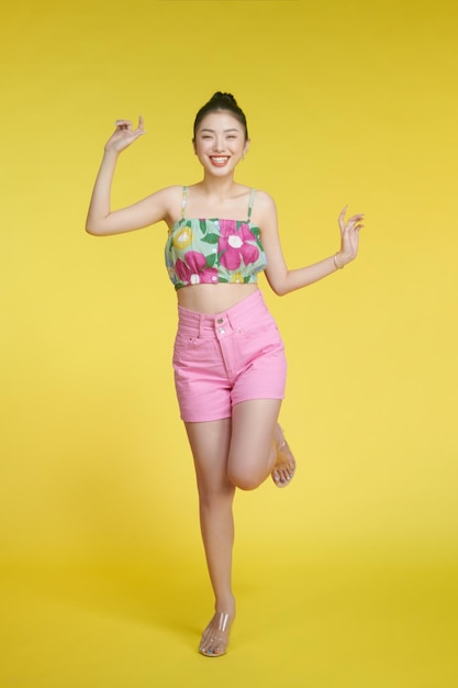 Hermosa mujer asiática con camiseta sin mangas de flores sobre fondo amarillo con una amplia sonrisa se regocija de tener el día libre