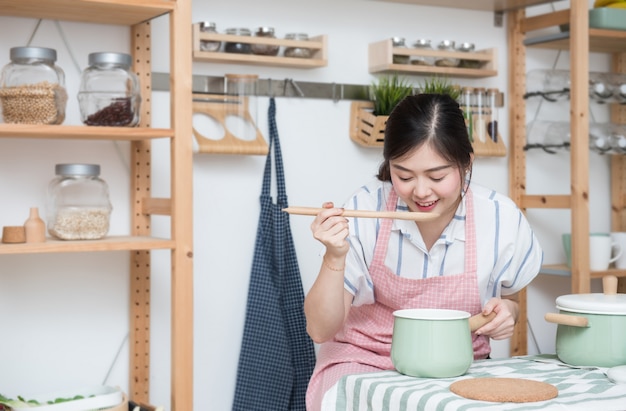 Hermosa mujer asiática cocinar y probar la sopa en la cocina