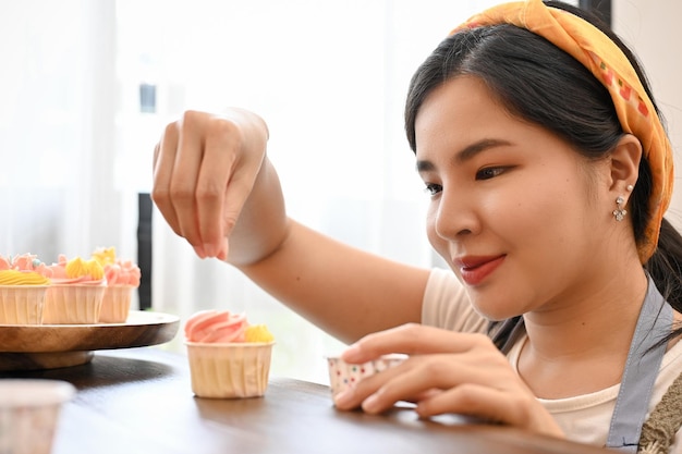 Hermosa mujer asiática decorando cupcakes caseros en la cocina