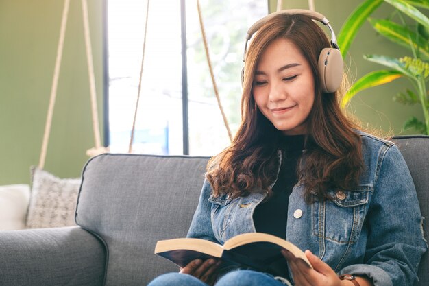 Una hermosa mujer asiática disfruta escuchando música con auriculares mientras lee un libro