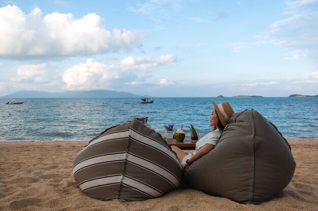 Una hermosa mujer asiática disfruta sentada y relajándose en una bolsa de frijoles en la playa