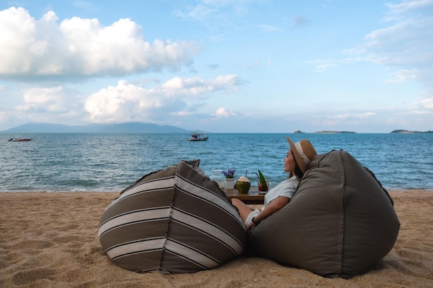 Una hermosa mujer asiática disfruta sentada y relajándose en una bolsa de frijoles en la playa