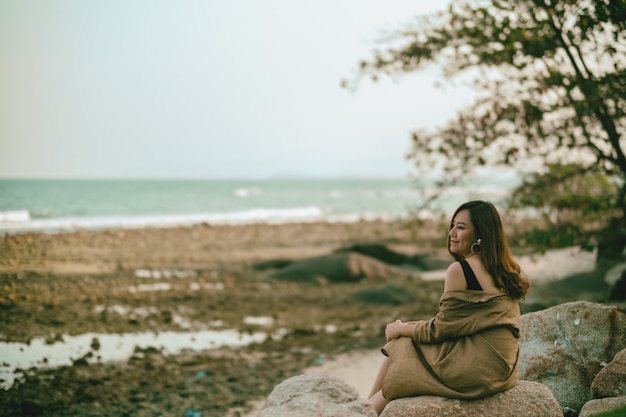 Una hermosa mujer asiática disfruta sentada en la roca junto a la orilla del mar