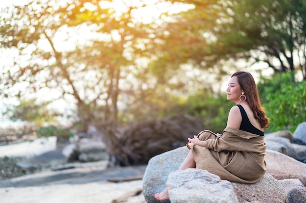 Una hermosa mujer asiática disfruta sentada en la roca junto a la orilla del mar