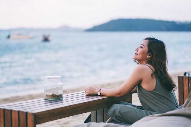 Una hermosa mujer asiática disfruta de sentarse y relajarse en la playa junto a la orilla del mar