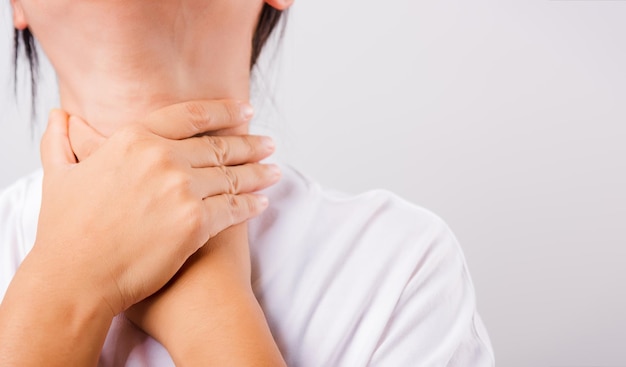 Hermosa mujer asiática dolor de garganta o problema de la glándula tiroides usando su mano tocando el cuello enfermo