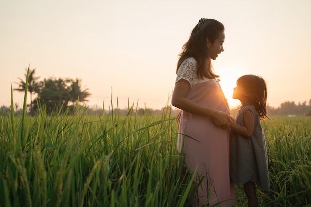 Hermosa mujer asiática embarazada con hija jugando en su barriga