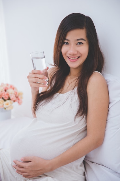 Hermosa mujer asiática embarazada sosteniendo un vaso de agua