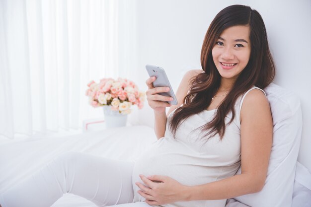 Hermosa mujer asiática embarazada usando un teléfono inteligente