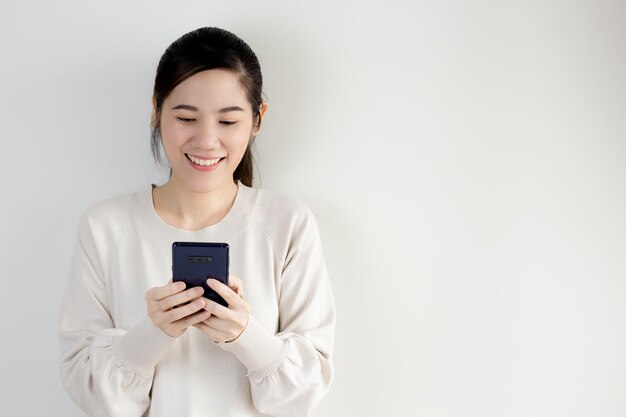 Hermosa mujer asiática está chateando o leyendo o comprando en línea en un teléfono inteligente con una sonrisa y felicidad