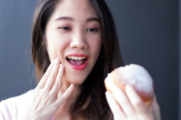 Hermosa mujer asiática está comiendo panecillo de donut con una sonrisa y felicidad durante la pausa para el café o el desayuno