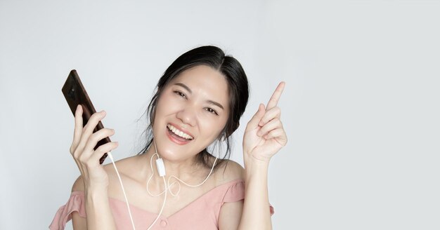 Una hermosa mujer asiática está escuchando música y apunta hacia arriba con una sonrisa, felicidad y baile.