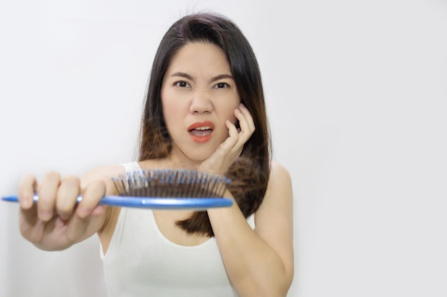 Hermosa mujer asiática está mirando su pérdida de cabello en un cepillo azul con preocupación y ansiedad