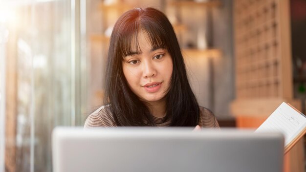 Una hermosa mujer asiática está trabajando remotamente en un café centrándose en su computadora portátil