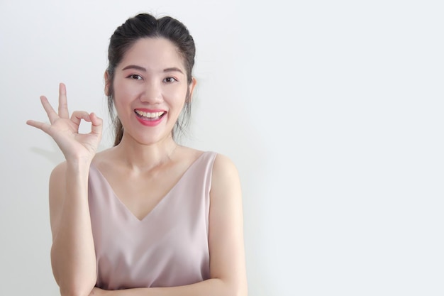 Hermosa mujer asiática hace un gesto de mano de acuerdo con una sonrisa para expresar la aprobación y decir que sí