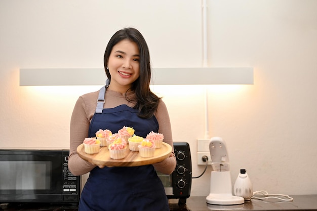 Hermosa mujer asiática haciendo cupcakes y mostrando cupcakes a la cámara