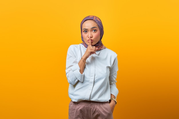 Hermosa mujer asiática haciendo el dedo en los labios boca gesto silencioso silencioso sobre fondo amarillo