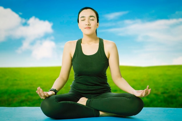 Hermosa mujer asiática haciendo ejercicio de yoga de respiración en el parque de verano