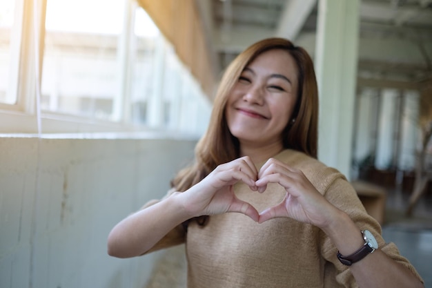 Una hermosa mujer asiática haciendo el signo de la mano del corazón con sentirse feliz