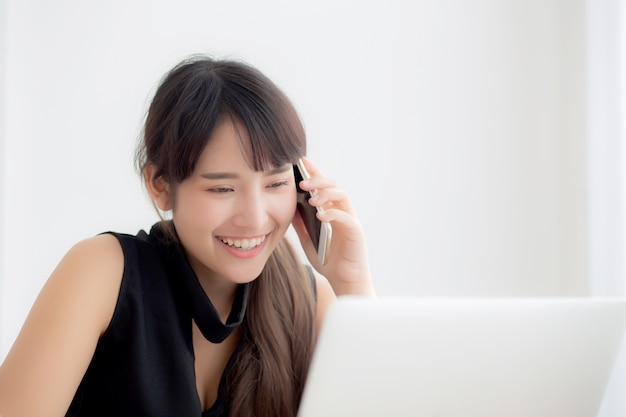 Hermosa mujer asiática independiente joven sonriendo trabajando en la computadora portátil y hablando de teléfonos inteligentes móviles