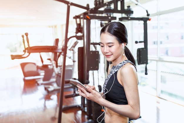 Hermosa mujer asiática joven con smartphone en gimnasio de fitness.