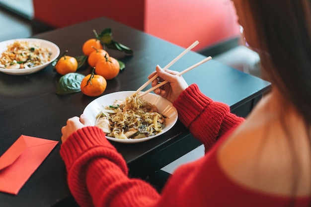 Foto hermosa mujer asiática joven sonriente en rojo comiendo fideos con palillos de bambú en el restaurante