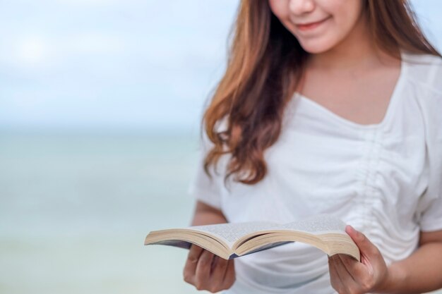Una hermosa mujer asiática leyendo un libro junto al mar