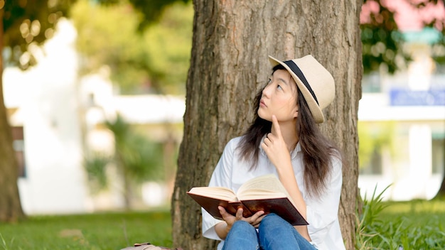 Una hermosa mujer asiática leyendo un libro bajo el pensamiento treeEmotion