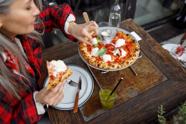 Hermosa mujer asiática madura está comiendo pizza en la terraza del café