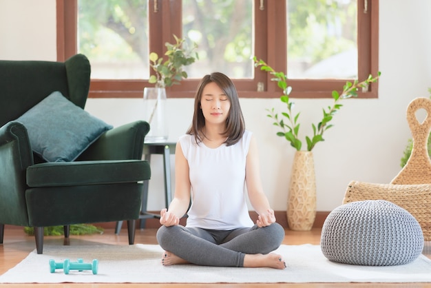 Hermosa mujer asiática mantiene la calma y medita mientras practica yoga en casa para un estilo de vida saludable