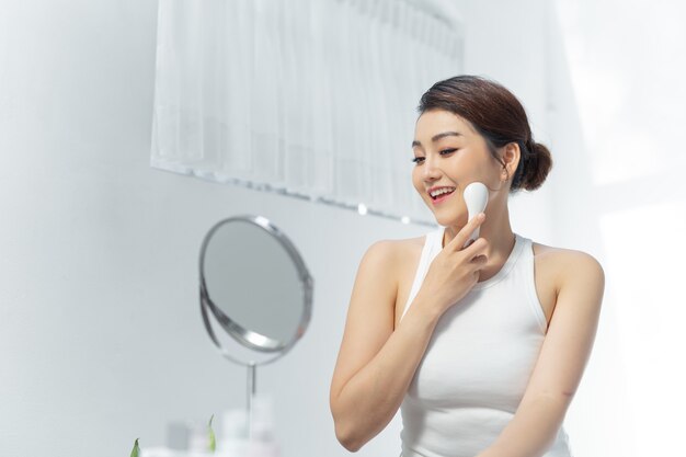 Hermosa mujer asiática y masaje facial eléctrico holdind de la mano aislado en la pared blanca