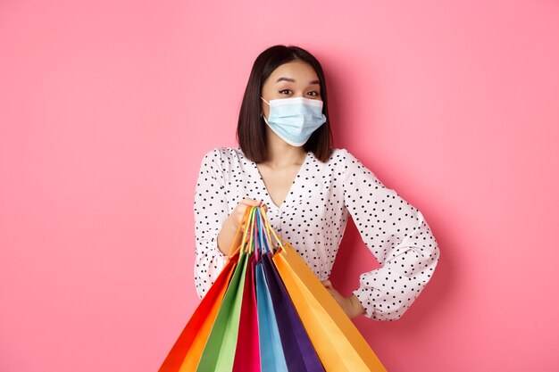 Hermosa mujer asiática en mascarilla dando bolsas de compras