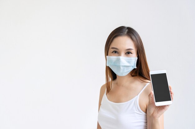 Hermosa mujer asiática con mascarilla médica con smartphone para espacio de copia sobre fondo blanco.