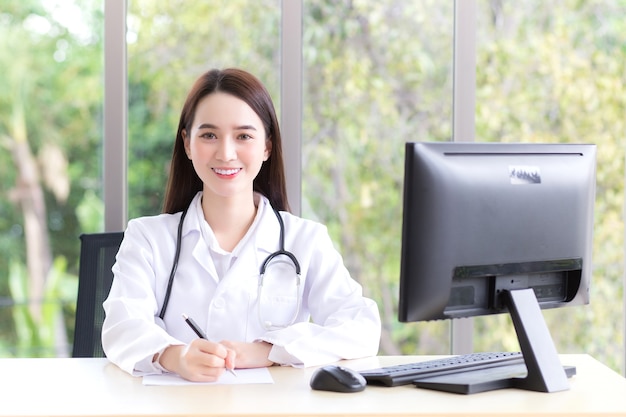 Hermosa mujer asiática médico que usa bata médica está trabajando en la sala de la oficina en el hospital